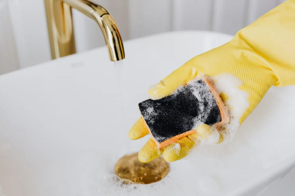 A homeowner rinsing a washable foam HRV filter under running water in a sink