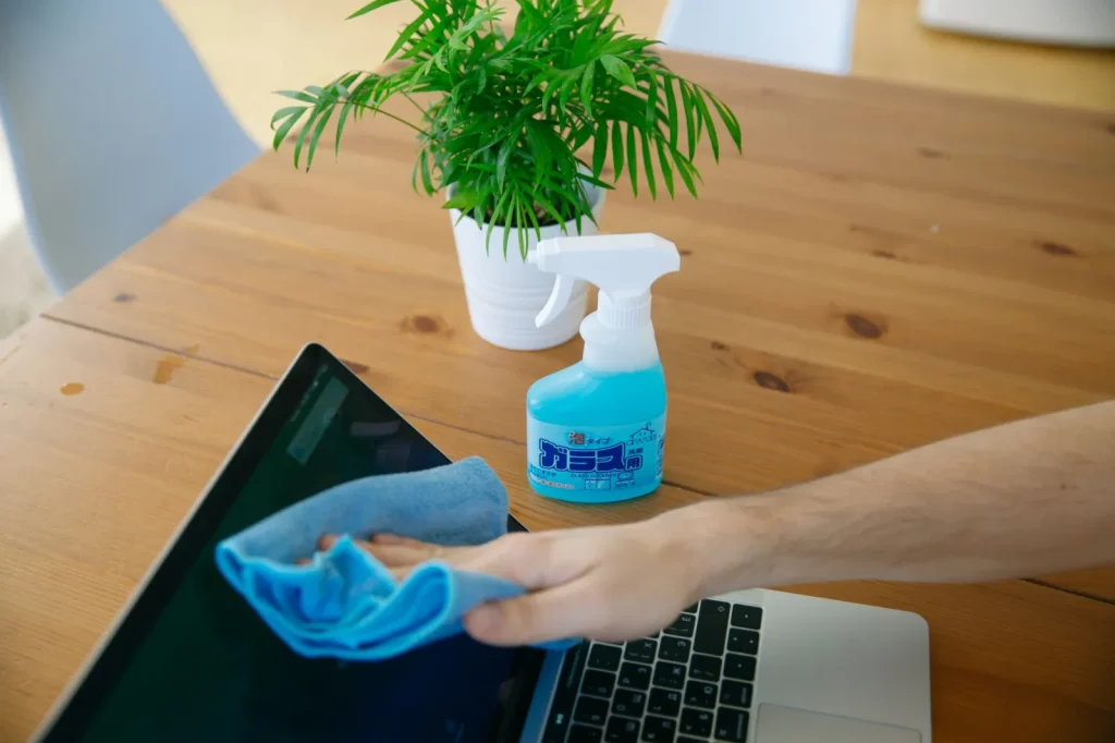 A hand wiping a wooden shelf with a damp microfiber cloth to capture settled dust