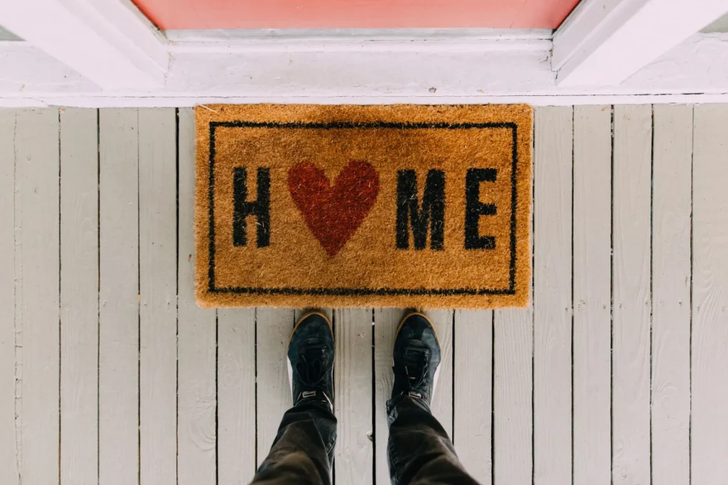 A coarse doormat and shoe rack at a home entryway used to stop tracked-in dust