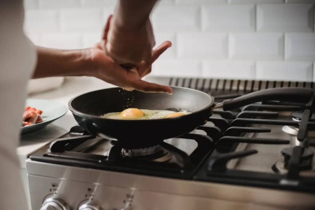 A range hood running on high over a pan searing on the back burner of a gas stove