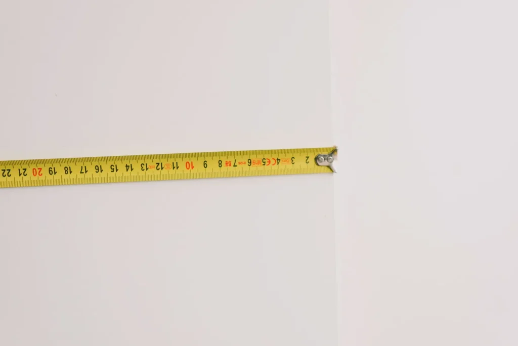 A person measuring ceiling height with a tape measure to calculate room volume