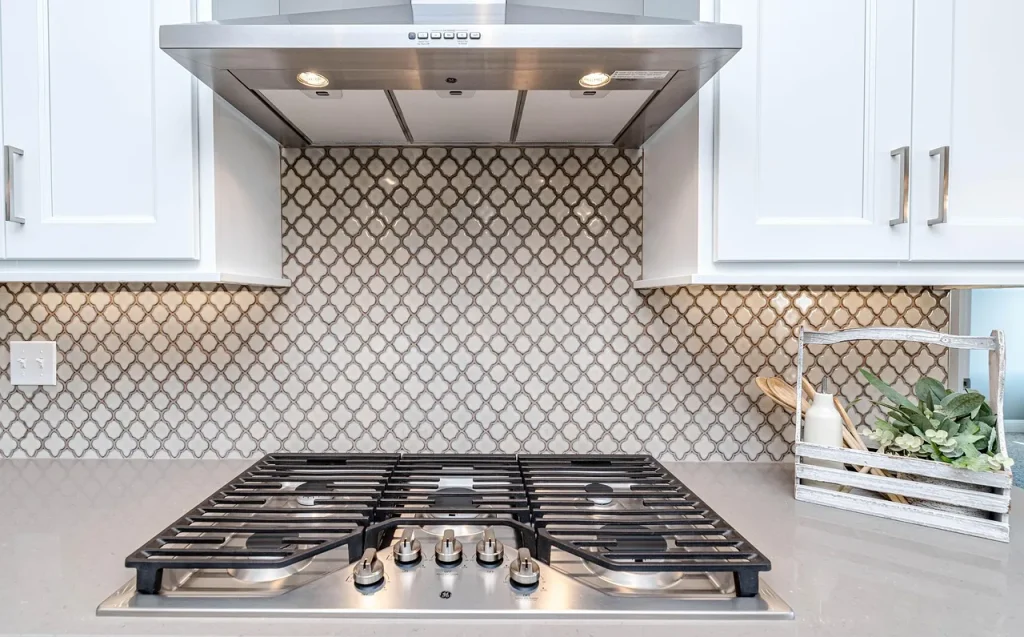 A stainless range hood running over a gas cooktop with a pot steaming below