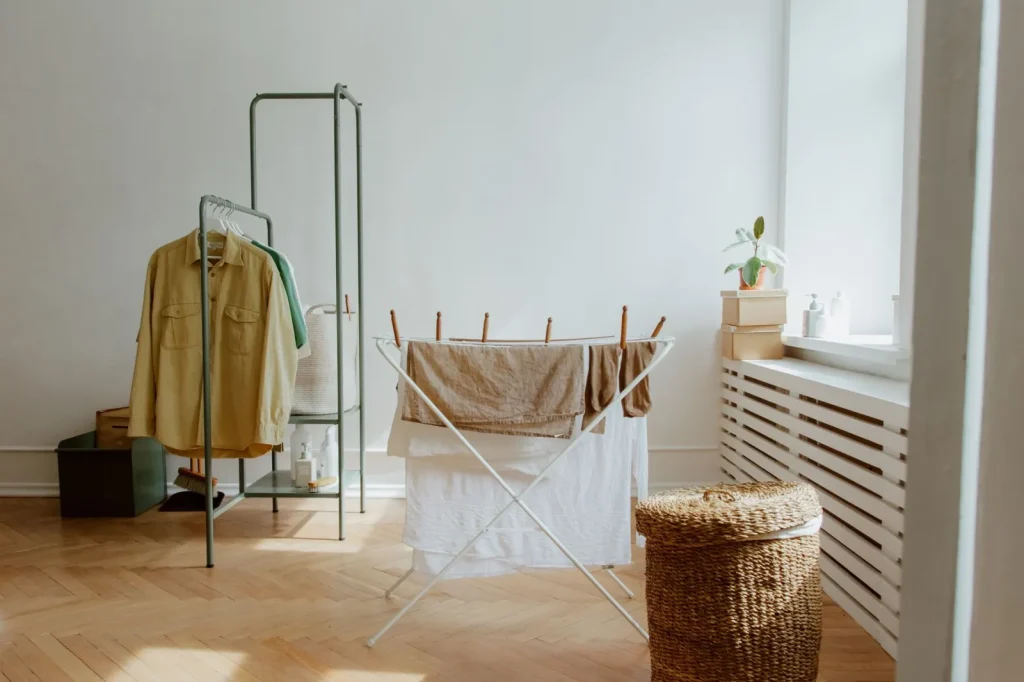 Clothes spaced on a drying rack in a small closed room with a dehumidifier running beside it