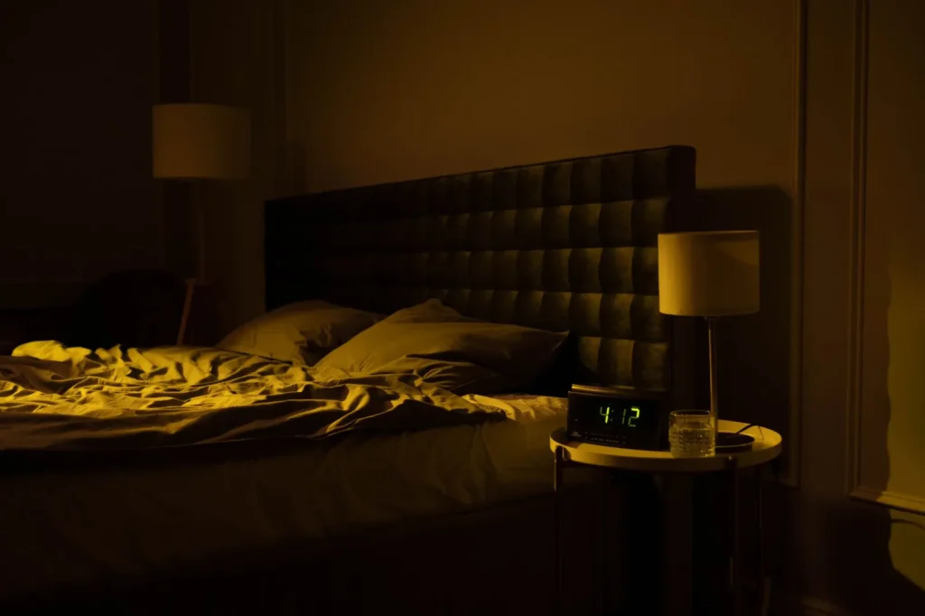 A cool-mist humidifier on a nightstand beside a bed, releasing a soft plume of vapor in a dim bedroom