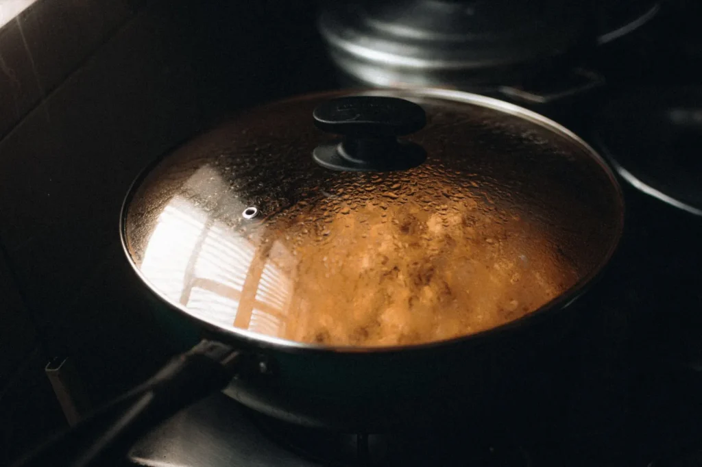A pot of water simmering with the lid off on a stovetop, releasing steam into the kitchen